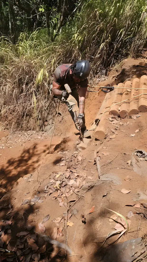 Renan cutting a log step into a steep red dirt trail with a chainsaw