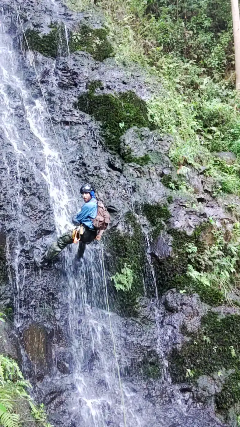 A rappeller in a helmet descending a tall waterfall on Kauai