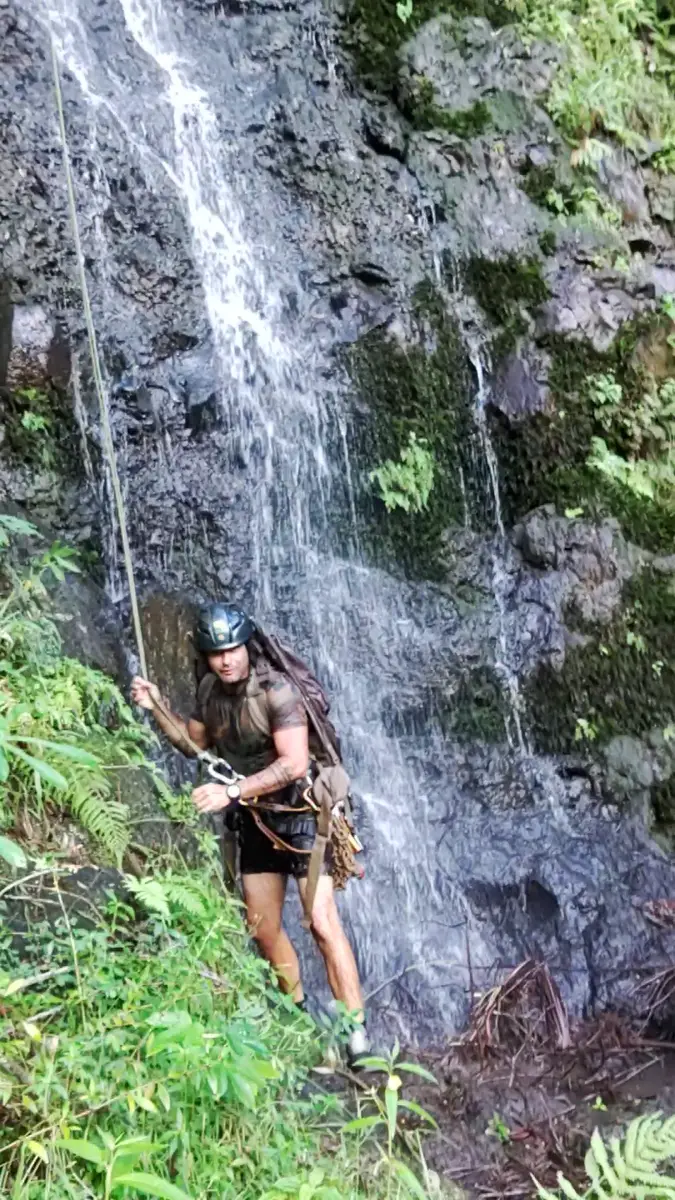 A rappeller in a helmet reaching the bottom of a waterfall, holding the rope