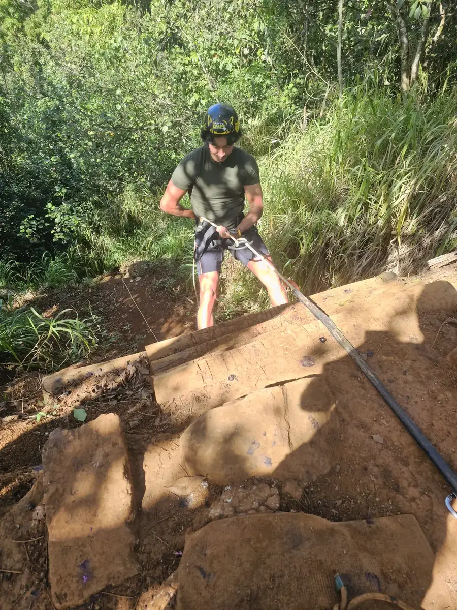 A crew member in a helmet and harness tied into a rope, working on a steep cut bank